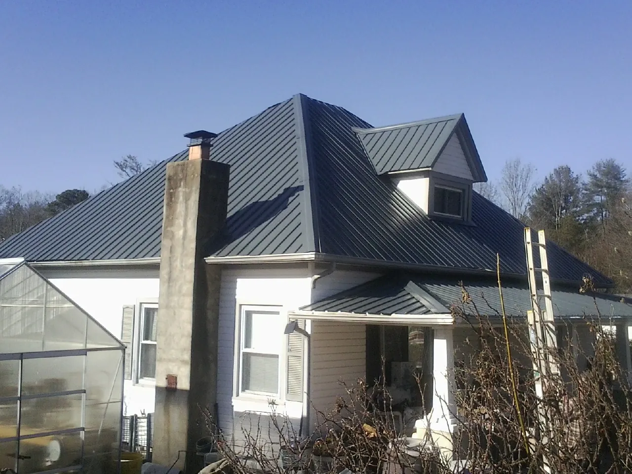 Dark blue standing seam metal roof on a white farmhouse with dormer — Slate & Tile Roof Repair by Roofing Brothers in North Stonington
