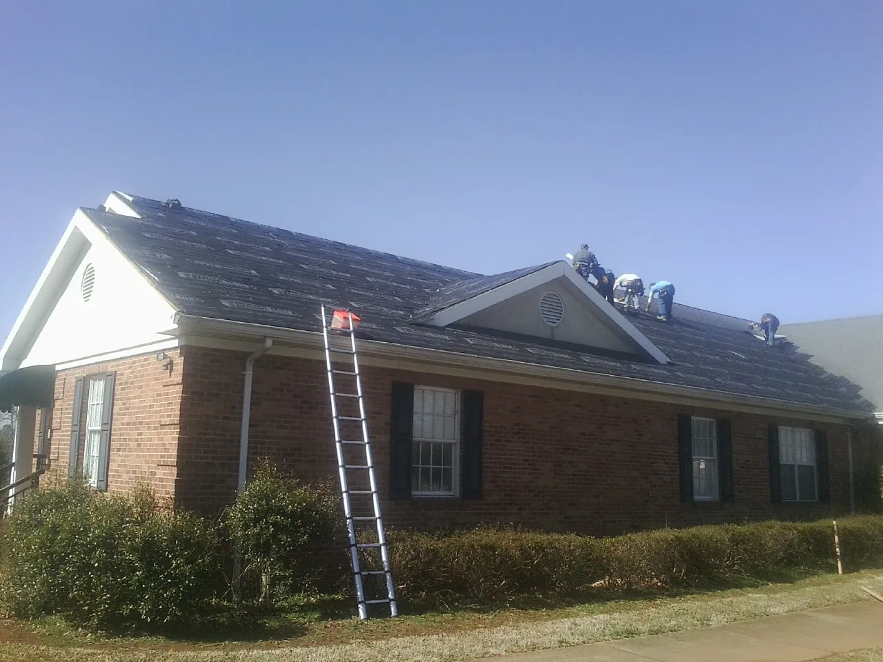 Crew tearing shingles off a brick ranch roof with a ladder set — Emergency Roof Repair work by our crew in North Stonington