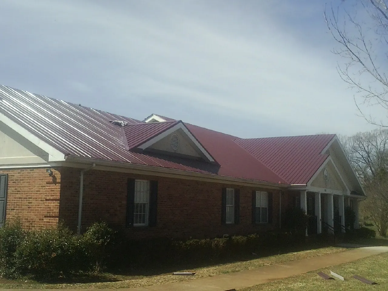 Red metal roof with gabled entries on a long brick building, from a Hail Damage Roof Repair job in North Stonington