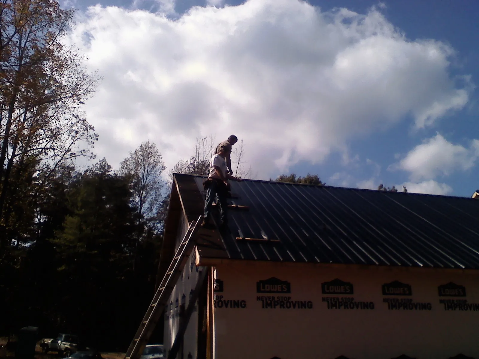 Roofer fastening dark metal panels high against a cloudy sky, from a Roof Inspection job in North Stonington