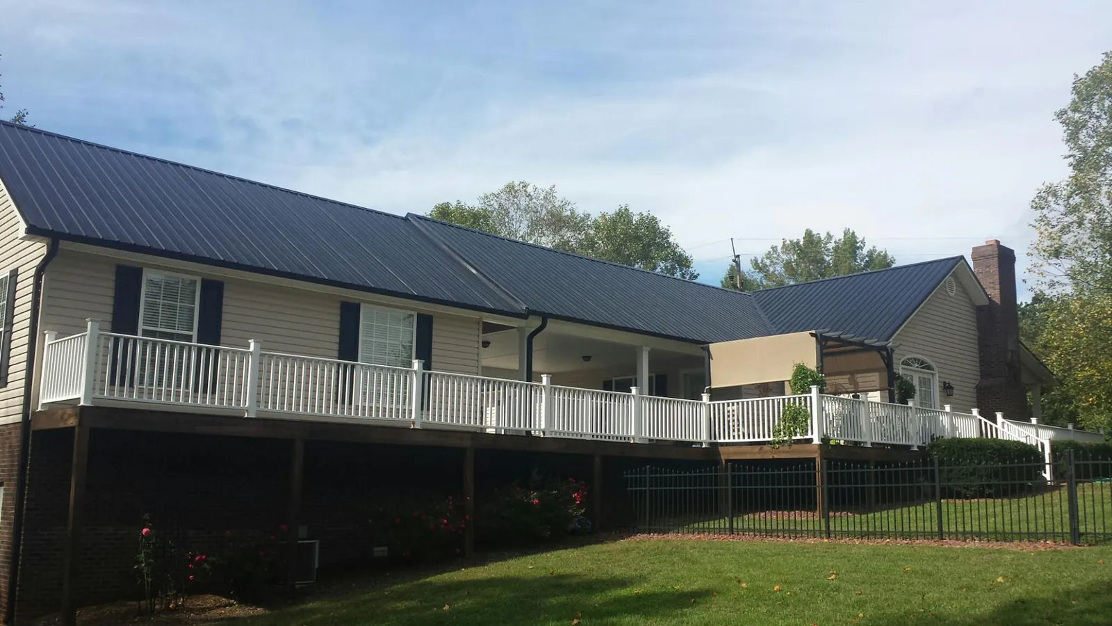 Black metal roof above a long white railed deck on a hillside home in North Stonington