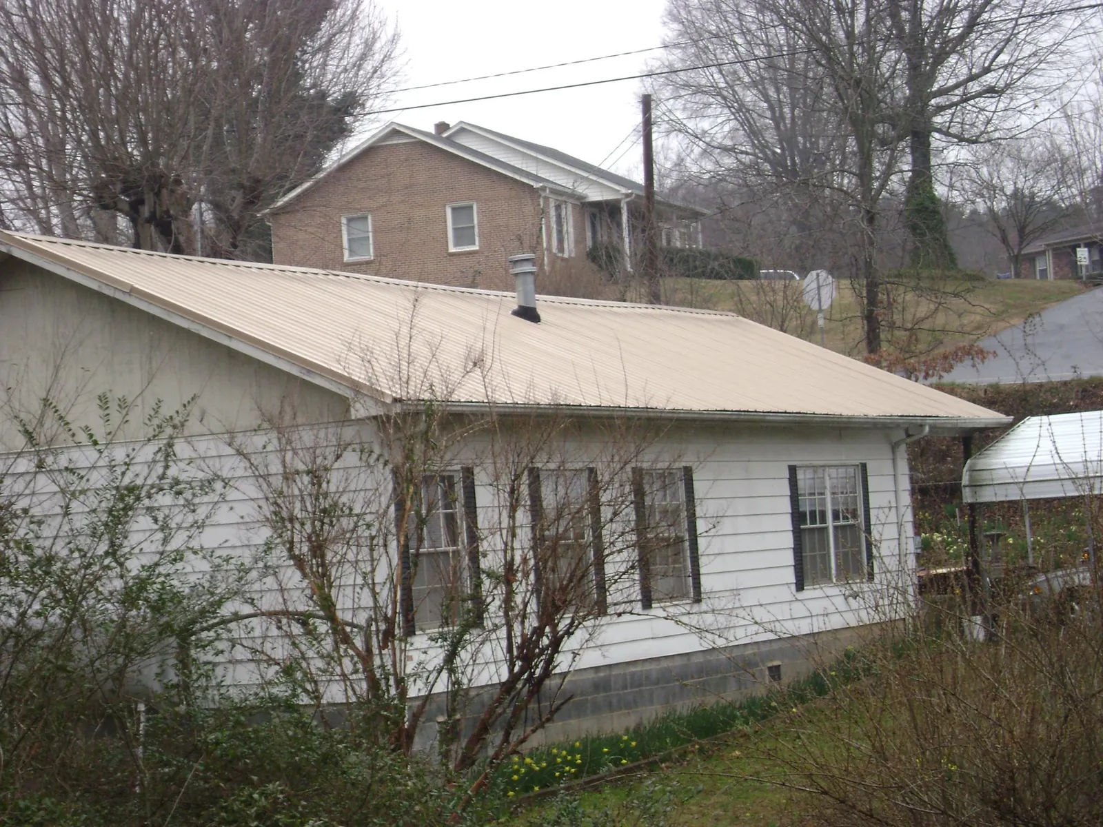 Tan metal roof on a white sided house set into a hillside — Commercial Roofing by Roofing Brothers in North Stonington